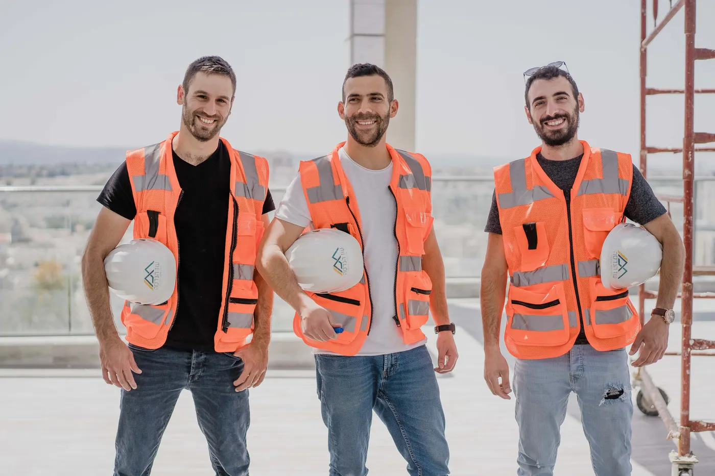 שלושת מהנדסי השטח של עוז הנדסה בקסדות ואפודים ממותגים על גג בניין